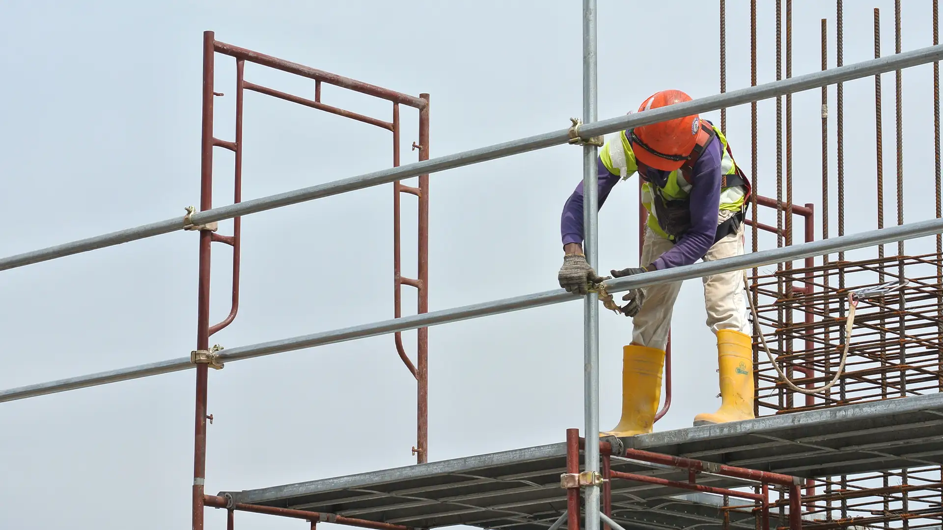 Bauarbeiter tragen Sicherheitsgurte und installieren auf der Baustelle in großer Höhe ein Gerüst.