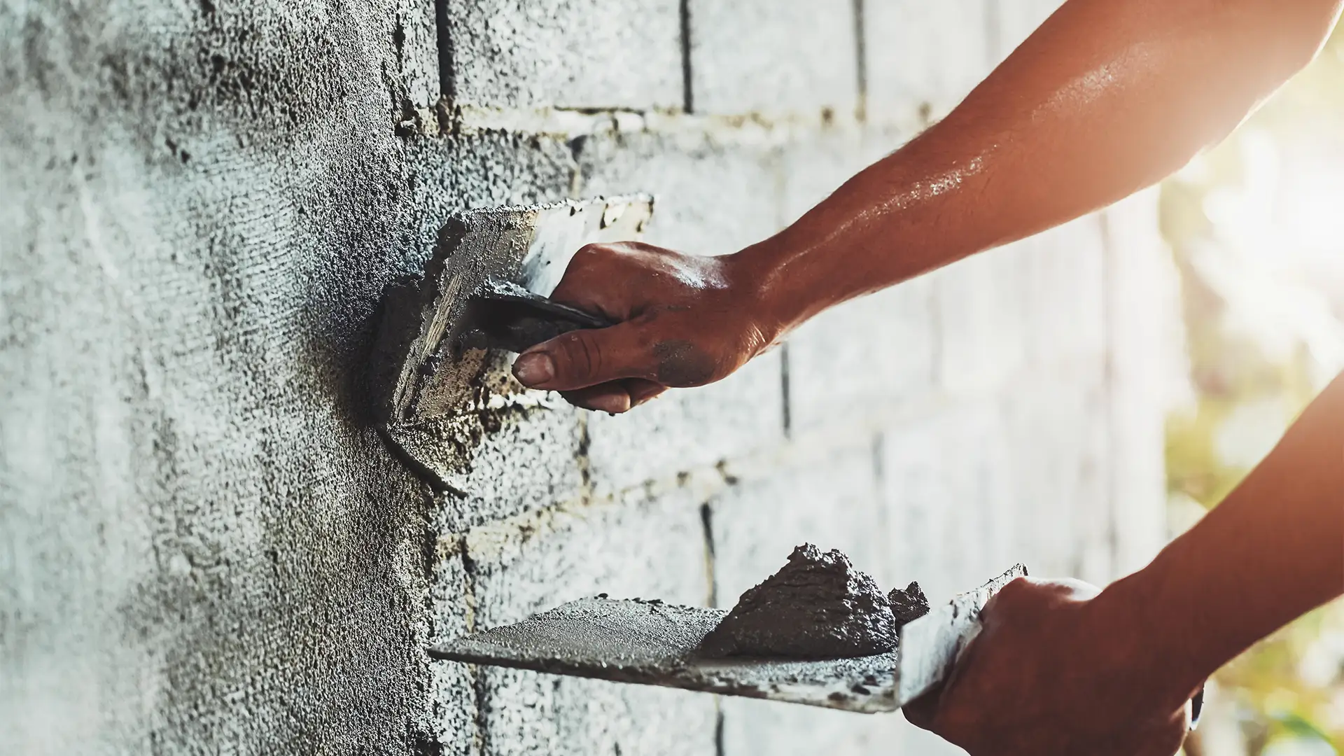 Nahaufnahme der Hand eines Arbeiters, der Zement an der Wand verputzt, um ein Haus zu bauen
